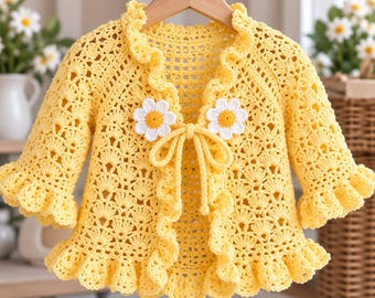 May include: A bright yellow crochet cardigan featuring an intricate openwork shell pattern, a ruffled collar, and ruffled sleeve cuffs. The garment is fastened at the center with a matching yellow tie adorned with two white and yellow daisy appliqués.