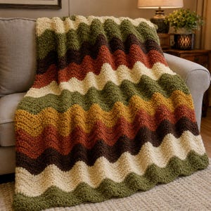 May include: A crochet blanket featuring a wavy chevron pattern in alternating horizontal stripes of cream, olive green, rust orange, mustard yellow, and dark brown. The textile has a thick, textured yarn construction with a soft, plush appearance.
