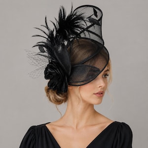 May include: A black fascinator hat featuring a structured mesh base, a large fabric flower, and upright feathers. The design includes a delicate netting veil overlay and curved structural elements, creating a sophisticated headpiece accessory.