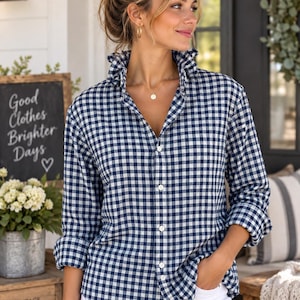 May include: A long-sleeved button-down shirt featuring a navy blue and white gingham check pattern. The shirt has a ruffled collar, a front button placket, and a single chest pocket. It is paired with plain white pants, creating a classic look.