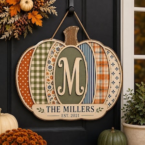 May include: A pumpkin-shaped wooden door sign featuring vertical panels with varied patterns including polka dots, gingham, floral, stripes, and plaid. A central oval displays the letter M, and a banner reads THE MILLERS EST. 2021.