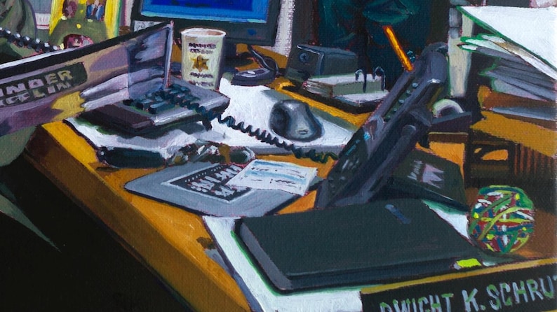 May include: An office desk scene with a laptop, telephone, and a coffee cup. A black computer mouse and a notepad are also visible. A colorful rubber band ball sits on the desk. The name "Dwight K. Schrute" is on a nameplate.