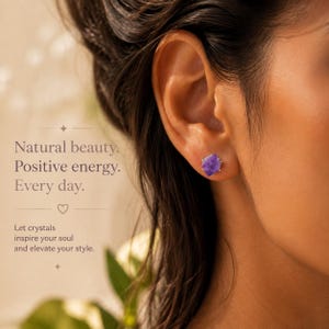 May include: A raw purple amethyst stud earring set in a metallic prong setting. The text on the image reads: Natural beauty. Positive energy. Every day. Let crystals inspire your soul and elevate your style. The earring is worn in an earlobe.