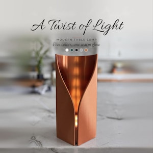 May include: A copper-colored table lamp with a curved, open-front cylindrical design that emits a warm glow from within. The text A Twist of Light, MODERN TABLE LAMP, and Five colors, one warm glow is visible above the lamp with five small circles.