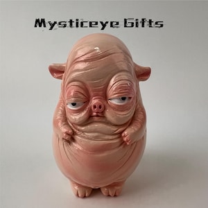 May include: A pale pink, hairless, rotund creature figurine with a pig-like snout, small ears, and heavy-lidded eyes. The surface has a glossy, wrinkled texture. Above the figure, the text Mysticeye Gifts is printed in a black, stylized font.