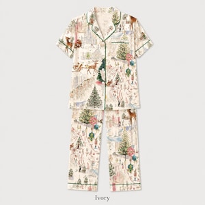 May include: A short-sleeved button-down pajama shirt and matching pants set in an ivory color. The fabric features a festive holiday print with illustrations of deer, Christmas trees, ornaments, and figures, accented by thin green piping trim.