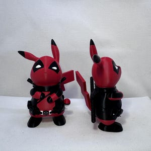 Puede incluir: Dos figuras impresas en 3D que representan un personaje híbrido de colores rojo y negro, con orejas puntiagudas, una máscara con parches oculares blancos, un cinturón negro y una cola en forma de rayo, vistas de frente y de lado.
