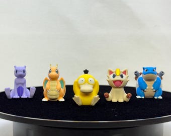 May include: A set of five small Pokémon character figurines arranged in a row. The figures include a purple Mewtwo, an orange Dragonite, a yellow Psyduck, a cream-colored Meowth, and a blue Blastoise, all standing in a seated or upright position.