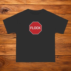 Puede incluir: Una camiseta negra de manga corta con un gráfico octogonal rojo en el pecho. El gráfico imita una señal de stop con un borde blanco y la palabra FLOCK impresa en letras mayúsculas blancas en el centro del octágono rojo.