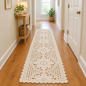 Può includere: Un lungo tappeto passatoia rettangolare all'uncinetto color bianco sporco, caratterizzato da un motivo floreale ripetuto con grandi fiori centrali e un bordo smerlato. Il design traforato è realizzato in filato, con una trama simile al pizzo.