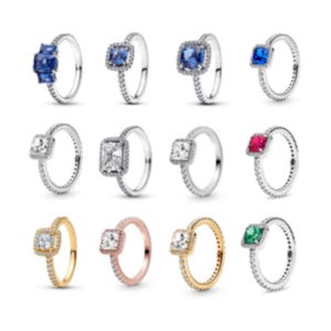 May include: A collection of twelve rings arranged in three rows. The rings feature various metal tones including silver, gold, and rose gold, with centre stones in blue, clear, red, and green, surrounded by small clear stones along the bands.
