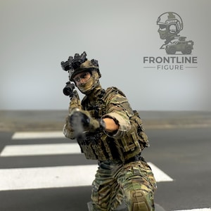 May include: A miniature soldier figurine in camouflage tactical gear, including a helmet with night vision goggles, a plate carrier vest, and a rifle held in a firing position. The figure is painted with realistic details and textures.