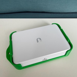 May include: A rectangular white electronic device with a silver logo on the top surface, secured within a bright green plastic mounting bracket. The device features a small horizontal indicator light on the front edge and a mounting hole on the side.