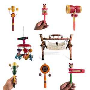 Puede incluir: Una colección de juguetes de madera hechos a mano que incluye varios sonajeros con coloridos detalles pintados, un móvil colgante con pequeñas figuras de elefantes y un marco de cuna en miniatura con una hamaca de tela, mostrando la artesanía tradicional.