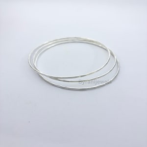 May include: Three thin, circular silver bangles with a hammered, textured surface. The bracelets are stacked slightly offset from one another, creating a layered appearance. The text Byranijewels is visible in small, dark lettering on the bottom.