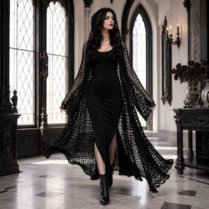 May include: A black floor-length dress with a scoop neckline and a high side slit, paired with a long-sleeved, open-front black crochet duster cardigan featuring an attached hood. The ensemble is completed with black pointed-toe ankle boots.