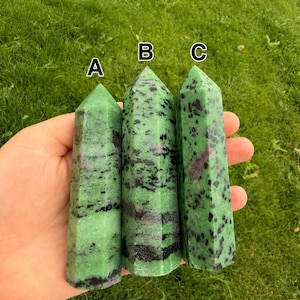May include: Three polished crystal towers labeled A, B, and C. Each tower is primarily green with black speckles and patches of deep magenta. The stones are hexagonal in shape with a pointed top, displaying natural mineral variations and textures.
