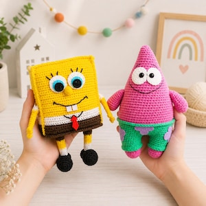 May include: Two handmade crochet dolls representing cartoon characters. One is a yellow square figure with blue eyes, a white shirt, and brown pants. The other is a pink cone-shaped figure with large eyes, a smiling mouth, and green shorts with purple flower patterns.