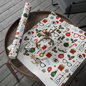 May include: White wrapping paper featuring a repeating pattern of red, green, and gold Christmas ornaments, candy canes, snowflakes, holly, and eye charts with the text E F P T O Z L P E D. A gift box wrapped in the same paper sits on the sheet.