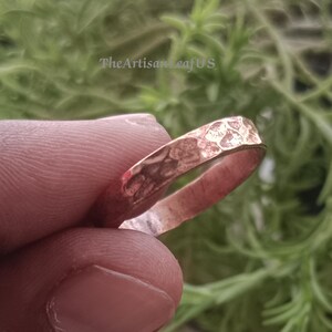 Peut inclure: Une bague en cuivre avec une surface martelée et texturée. L'anneau présente un aspect métallique irrégulier et réfléchissant avec une teinte brun-rouge chaude. Le texte TheArtisanLeafUS est visible en arrière-plan derrière la bague.