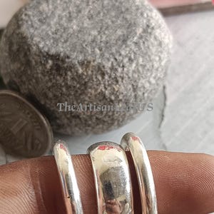 May include: Three silver-toned rings with smooth, polished surfaces. The centre ring is wider than the two thinner rings flanking it. The rings are displayed together, showcasing their reflective metallic finish and simple, rounded band design.