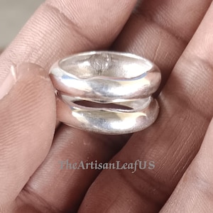May include: A polished silver ring featuring a double-band design with a smooth, rounded surface and a central open gap. The metal has a reflective finish, and the text TheArtisanLeafUS is visible in the lower portion of the image.
