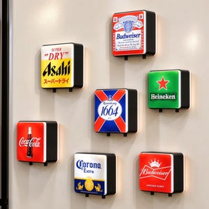Könnte beinhalten: Eine Sammlung von sieben quadratischen, beleuchteten Wandleuchten mit verschiedenen Getränkemarkenlogos, darunter Budweiser, Asahi Super Dry, Kronenbourg 1664, Heineken, Coca-Cola, Corona Extra und ein zweites Budweiser-Design in Rot und Weiß.
