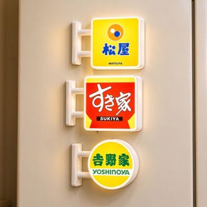 Peut inclure: Trois enseignes lumineuses murales présentant des marques de restaurants japonais. L'enseigne du haut est jaune avec le logo bleu Matsuya. Celle du milieu est rouge avec le texte blanc Sukiya. Celle du bas est un cercle jaune avec le texte vert Yoshinoya.