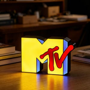 以下が含まれることがあります： 鮮やかな黄色のブロック体のMの文字に、太字で赤いスタイリッシュなTVの文字が重なった、立体的なMTVロゴの照明付きサイン。サインの側面は柔らかな青い光で照らされており、表面に輝くような効果を生み出しています。