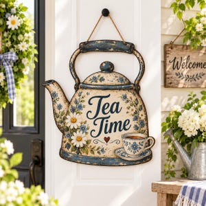 Könnte beinhalten: Ein dekoratives Wandschild in Teekannenform mit abgenutztem blau-cremefarbenem Finish. Es zeigt gemalte weiße Gänseblümchen, blaue Blumen, ein kleines rotes Herz und den Schriftzug Tea Time in dunkelblauer Schreibschrift sowie eine passende Tasse.