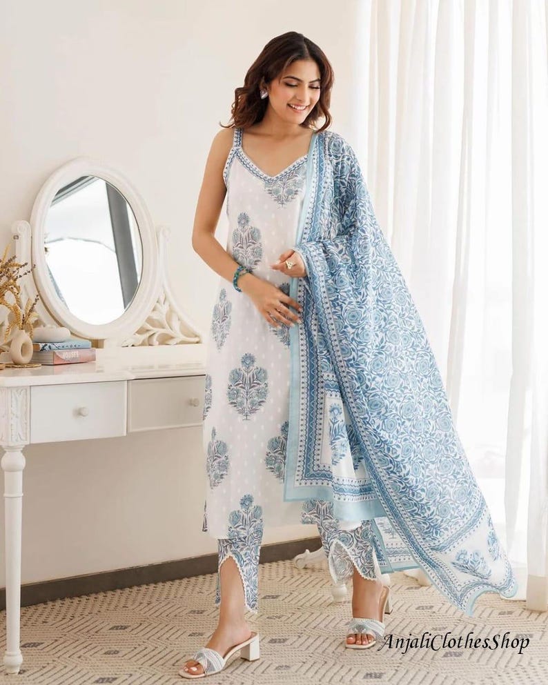 May include: A white sleeveless kurta with a blue floral block print, paired with matching cropped trousers featuring a V-shaped hem detail and a coordinating blue and white floral print dupatta draped over the shoulder and arm.