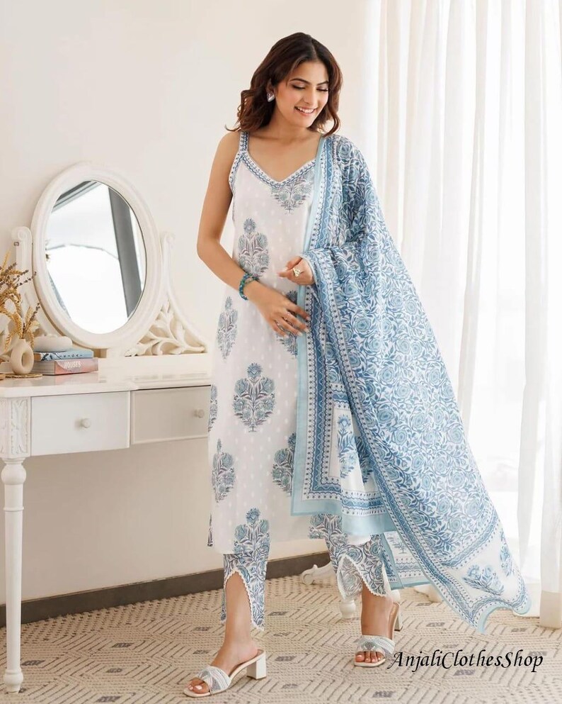 May include: A white sleeveless kurta with a blue floral block print, paired with matching cropped trousers featuring a V-shaped hem detail and a coordinating blue and white floral print dupatta draped over the shoulder and arm.