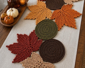 May include: A collection of crocheted table decorations featuring various maple leaf shapes and circular mats in autumn colors including rust, dark brown, olive green, and tan, arranged in a decorative pattern on a light beige fabric table runner.