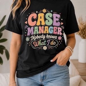 以下が含まれることがあります： 「CASE MANAGER Nobody knows What I do」というレトロなフォントのテキストと、ピンク、黄色、青、紫の色合いの小さな花、ハート、星のアイコンが描かれたカラフルなグラフィックプリントが特徴の黒い半袖Tシャツ。