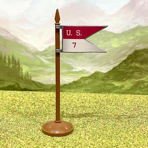 May include: A miniature brown flagpole with a pointed finial and a circular base. Attached to the pole is a swallowtail flag featuring a horizontal split design with a red top section labelled U. S. and a white bottom section with the number 7.