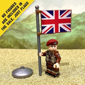Puede incluir: Una bandera de plástico en miniatura con el diseño de la Union Jack unida a un poste gris con una base circular. La bandera es rectangular con colores rojo, blanco y azul. El texto NO FIGURES ARE INCLUDED IN THE SALE, JUST FLAGS es visible.