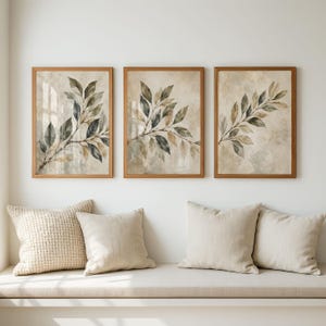 May include: Three rectangular wall art prints in light wood frames, each featuring a watercolour-style botanical illustration of leafy branches in shades of muted green, brown, and grey against a textured, neutral-toned background.