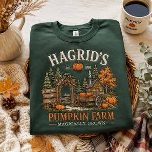 May include: A dark green crewneck sweatshirt featuring an embroidered graphic of a pumpkin farm. The design includes a wooden cabin, a cart, trees, and text that reads: HAGRID'S est. 1981 PUMPKIN FARM MAGICALLY GROWN, with signs for PUMPKINS, POTIONS, & PLANTS.