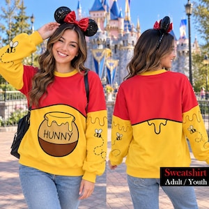 May include: A red and yellow long-sleeve sweatshirt featuring a graphic of a honey pot labeled HUNNY on the front, with small bee illustrations on the sleeves. The design includes a dripping honey pattern and is paired with black mouse ears.