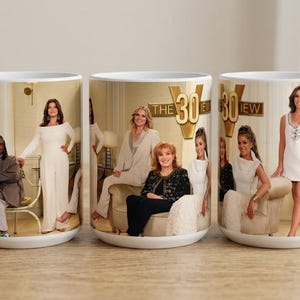 Peut inclure: Trois tasses en céramique blanche présentant une photographie de groupe de l'émission télévisée The View. Les tasses affichent le logo de l'émission avec le nombre 30 et divers membres de l'équipe vêtus de blanc, noir et tons neutres.