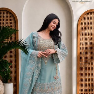 May include: A light blue salwar suit featuring intricate silver embroidery, beadwork, and sequins on the bodice and hem. The ensemble includes a matching sheer dupatta with scalloped edges and detailed floral embroidery, paired with wide-leg trousers.
