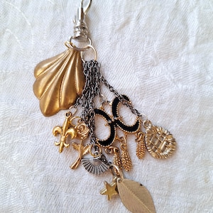 May include: A gold and silver charm keychain with a variety of charms, including a seashell, a fleur-de-lis, a rose, a fan, a star, a leaf, and a woven basket.