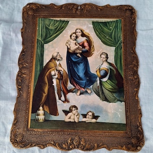 May include: A framed religious print featuring a depiction of the Virgin Mary holding the baby Jesus, surrounded by figures and cherubs. The artwork is set against a backdrop of green curtains and a cloudy sky, within a decorative brown frame.