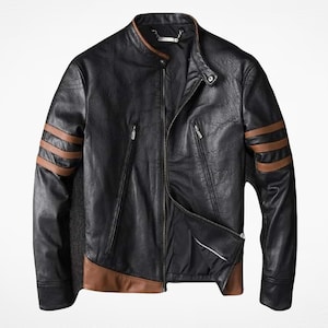 Könnte beinhalten: Eine schwarze Jacke mit Stehkragen, drei horizontalen braunen Streifen an jedem Ärmel und einem braunen Einsatz am unteren Saum. Die Jacke verfügt über einen zentralen Reißverschluss, zwei diagonale Reißverschlusstaschen und einen Druckknopf.