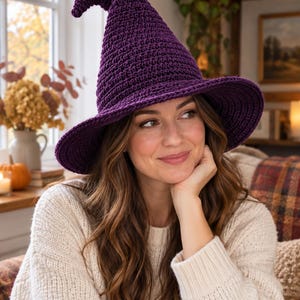May include: A deep purple crocheted witch hat featuring a tall, pointed crown with a slight curve at the tip and a wide, circular brim. The hat is constructed from textured yarn with a consistent stitch pattern throughout the entire piece.