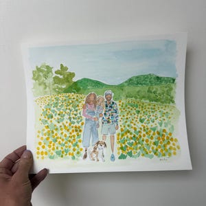 May include: Watercolor painting of a family of four and a dog in a field of yellow flowers. The family is standing in front of a green hill and blue sky. The painting is held by a hand.