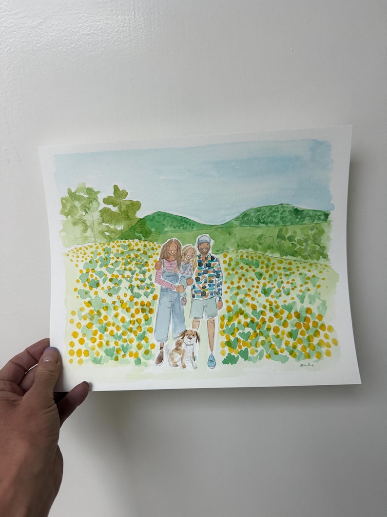 May include: Watercolor painting of a family of four and a dog in a field of yellow flowers. The family is standing in front of a green hill and blue sky. The painting is held by a hand.