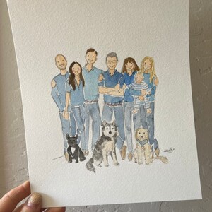 May include: Watercolor portrait of a family and their three dogs. The figures are dressed in shades of blue, with the dogs in front. The artwork is on white paper, held by a hand with glittery nail polish.