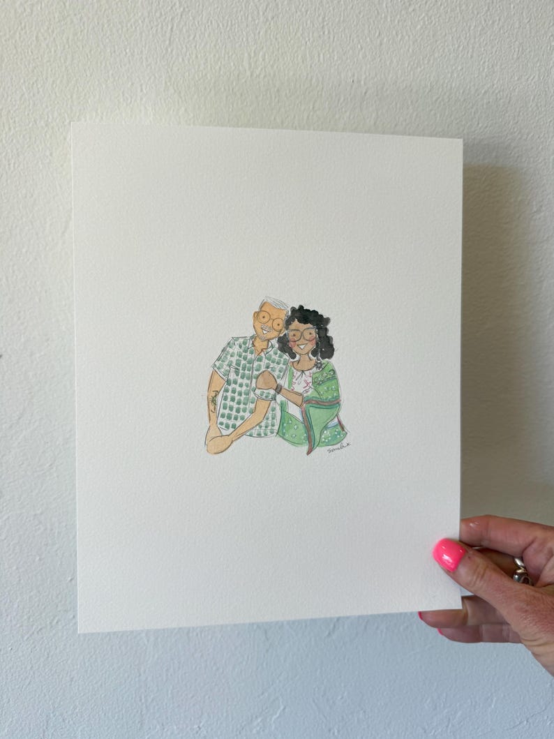 May include: Watercolor portrait of a couple, featuring a man in a green patterned shirt and a woman in a green sari. The artwork is on white paper, held by a hand with pink nail polish.
