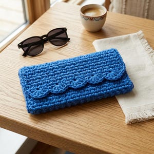 May include: A rectangular blue crochet clutch featuring a textured stitch pattern and a scalloped edge flap closure. The accessory is crafted from yarn and displays a consistent vibrant blue color throughout its entire construction.